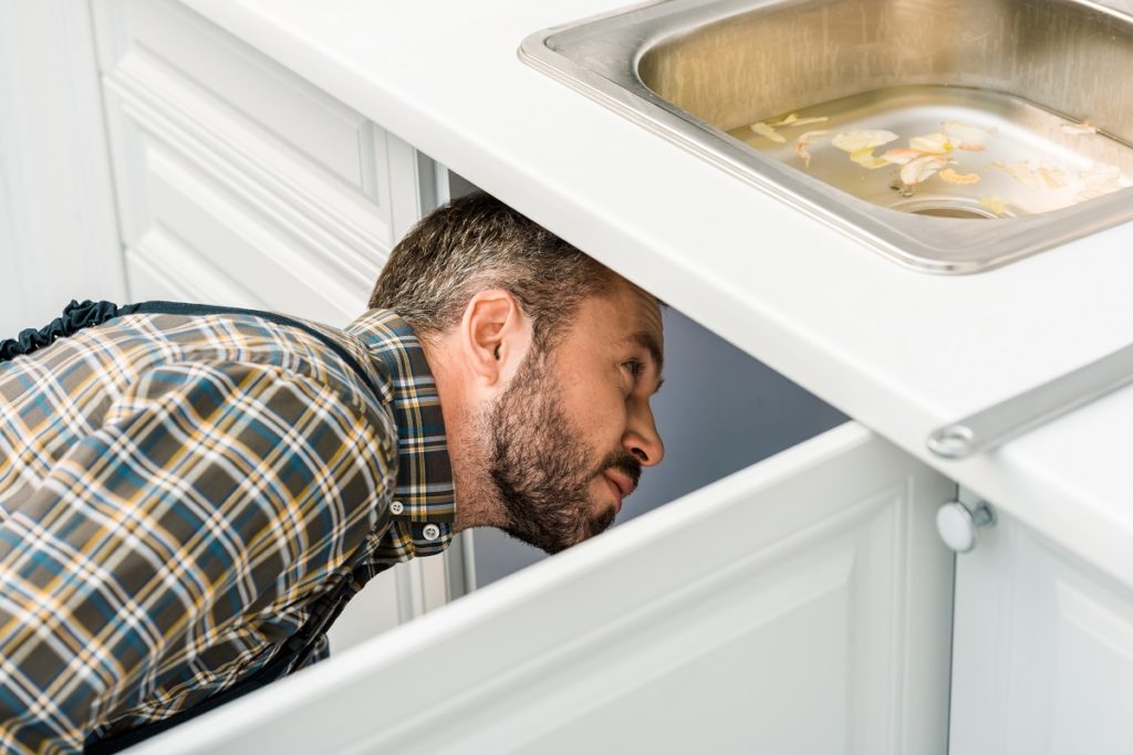 plumber looking under broken sink in kitchen