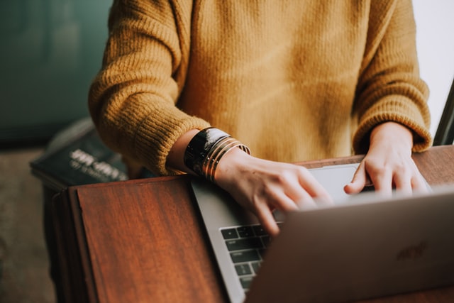 someone in a sweater typing on a laptop
