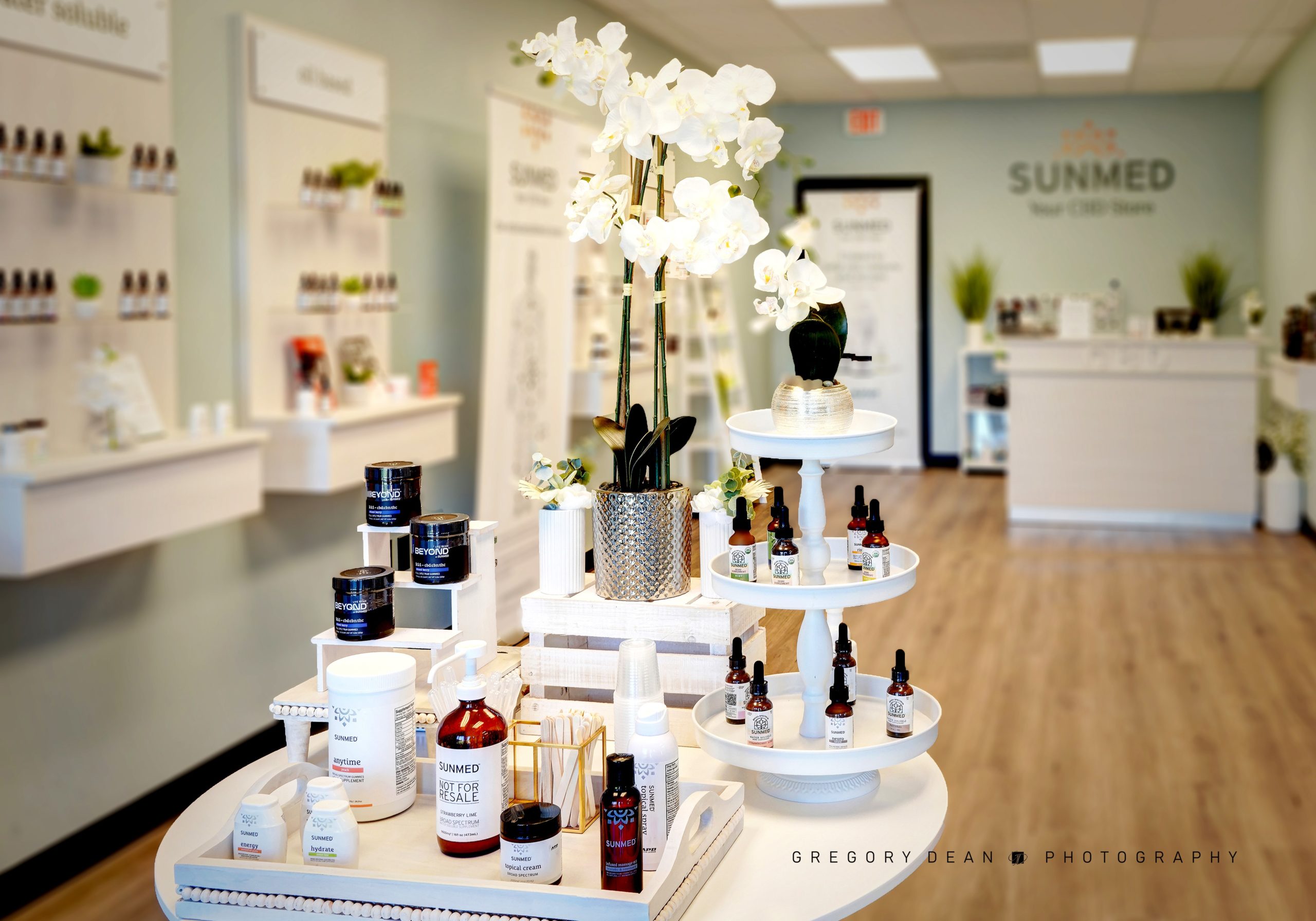 Sunmed Your CBD Store - Keizer and Salem locations - picture of the interior of the Keizer Store showing a beautiful white orchid, peaceful light green walls and wood floor - white tables and shelves with products in bottles and other containers.
