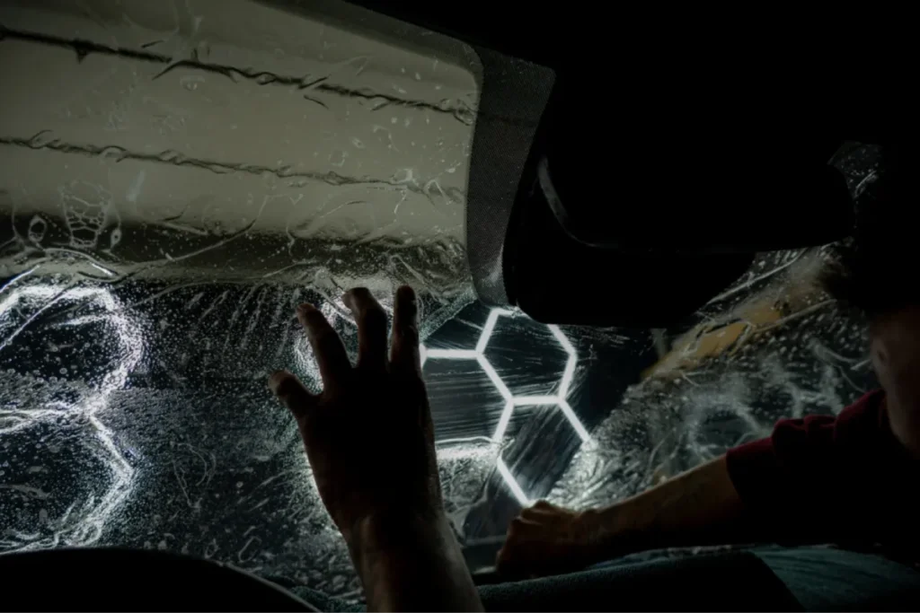 Hand smoothing film onto a wet car windshield during window tinting installation.