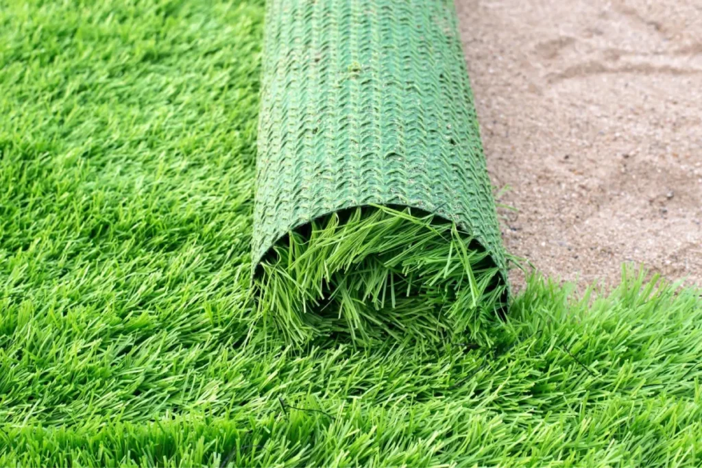 Roll of green commercial turf being installed over prepared ground.
