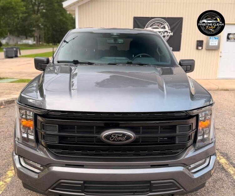 Direct head-on view of a dark gray Ford pickup truck parked outdoors in front of a building.
