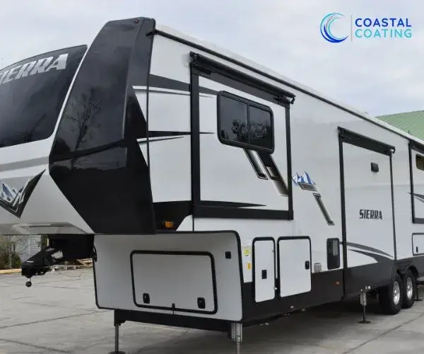 Side view of a white fifth-wheel RV trailer with black graphics and slide-outs extended.