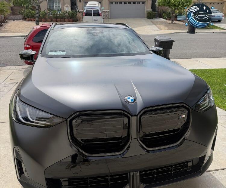 Front close-up view of a matte black BMW SUV parked on a residential driveway.