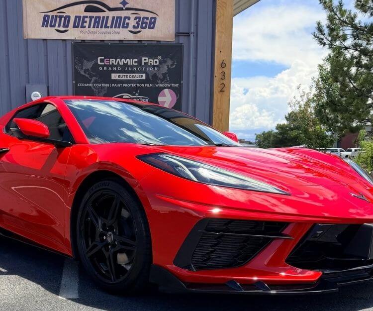 Close-up front three-quarter view of a glossy red Chevrolet Corvette parked outside an auto detailing shop.